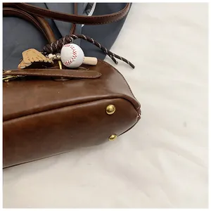 Detail of coffee brown leather shell bag with gold hardware and baseball charm