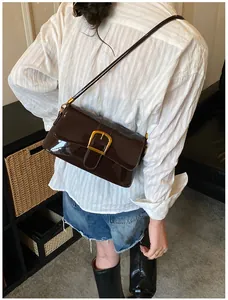Detailed shot of dark brown patent leather baguette bag with gold horseshoe buckle clasp