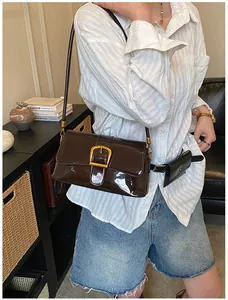 Détail du sac en cuir verni marron foncé brillant avec boucle dorée et breloque