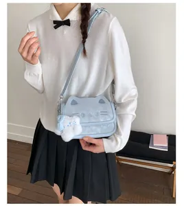 Detail of light blue cat-shaped crossbody bag with ear details and a white plush charm