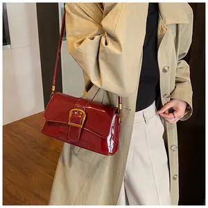 Detail of dark red patent leather baguette bag featuring a large gold buckle and strap