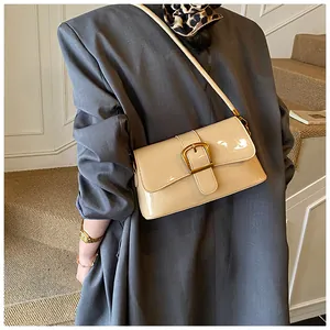 Detail of a beige patent leather baguette bag with a large gold square buckle on the flap