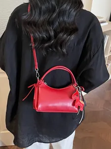 Minimalistische rote Handtasche mit Pferdeanhänger, getragen von einem Model zu Hause