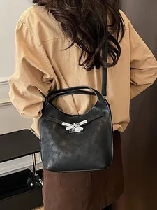 Elegant black bucket bag with silver bow buckle worn by a model in a minimalist setting