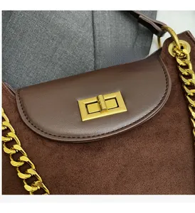 Close-up of golden metal lock and chain strap on a brown suede baguette handbag