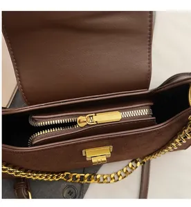 Close-up of brown suede baguette bag featuring smooth metal zipper and gold chain detail