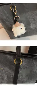 Macro shot of fluffy white plush doll charm with metal hardware on grey tote bag