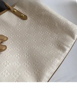 Detail of beige tote bag showing houndstooth embossed texture and leather handle