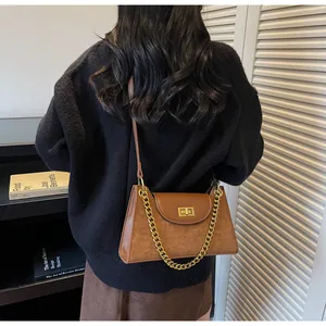 Close-up of brown suede patchwork handbag with gold chain strap and metal lock