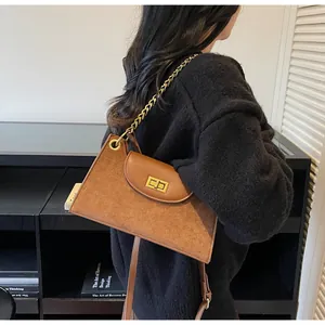 Detail of a brown suede crossbody bag with gold chain and metal buckle closure