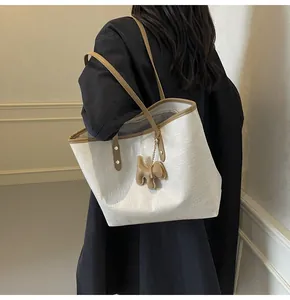 Detail view of cream leather tote bag with brown straps and cute puppy charm on model