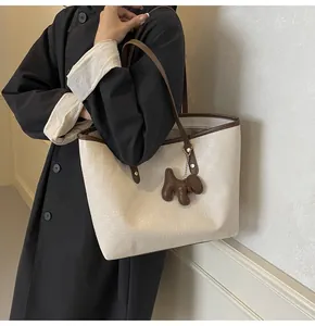 Detail of cream tote bag with monogram texture, brown leather trim and dog charm