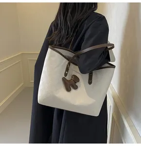 Detail of off-white quilted tote bag with brown leather handles and bear charm