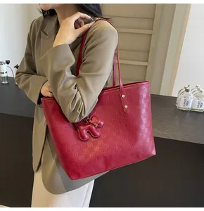 Detail of red checkered tote bag with leather texture and elephant pendant on shoulder