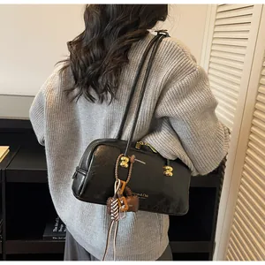 Detalle de bolso Boston negro con logo dorado y un colgante decorativo multicolor