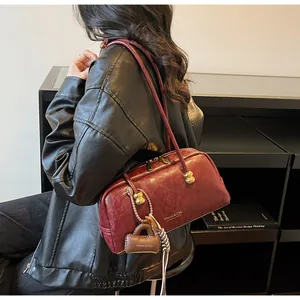 Detalle del bolso boston de cuero burdeos con herrajes dorados y amuleto de marca