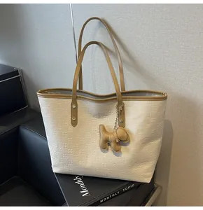 Close-up of textured beige tote bag with brown handles and a cute dog charm attachment