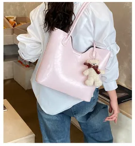 Detail of pink glossy leather tote bag featuring a cute plush bear charm on the strap