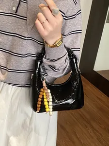 Glossy black pleated moon bag with beaded charm accessory shown in a lifestyle indoor setting