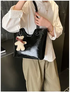 Detail of a black patent leather tote bag with a cute plush bear charm on the shoulder strap