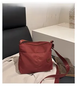 Detailed close-up of a burgundy nylon crossbody bag with multi-zipper layers and logo