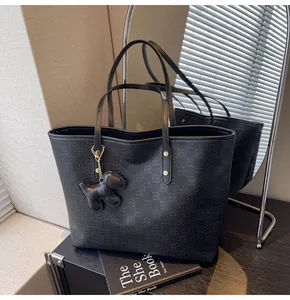Detail of black embossed checkerboard tote bag with a dog-shaped charm and gold hardware