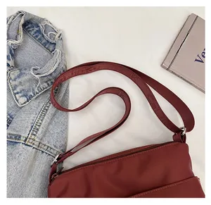 Detail of burgundy nylon crossbody bag featuring wide jacquard strap with relief lettering