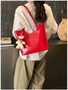 Detail view of glossy red tote bag with wavy edges and a cute white bear pendant
