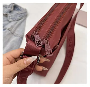 Detail of smooth double zippers and branded wide strap on dark red nylon crossbody bag