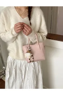 Gros plan d'un sac seau en cuir rose avec pendentif en peluche sur un pull blanc