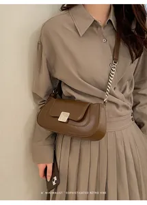 Detail of a minimalist brown baguette bag with a brushed metal buckle and leather chain strap