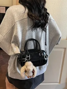 Sac baguette en cuir verni noir avec charme lapin en peluche porté par modèle