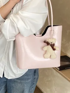 Pink glossy leather tote bag with cute plush bear pendant on a long shoulder strap