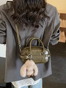 Mini sac Boston minimaliste vert olive avec breloque en peluche porté par un mannequin