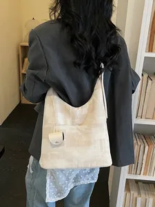 Large beige woven hobo tote bag with wide strap and matching pouch in a library setting