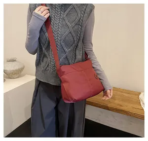 Close-up of burgundy nylon crossbody tote bag with a wide branded shoulder strap