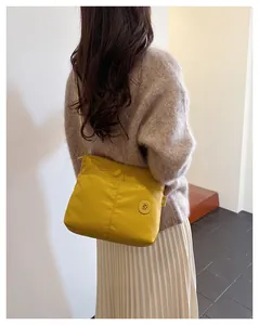 Detail view of the yellow nylon tote bag with brand logo shown on a brown sweater background