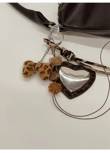 Λεπτομέρεια από λεοπάρ φιόγκο, βελούδινες μπάλες και καθρέφτη καρδιά σε καφέ τσάντα