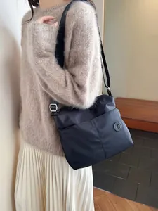 Black nylon crossbody tote bag with adjustable strap worn with a beige sweater