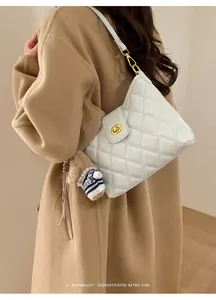 Detailed side view of white quilted leather underarm bag with gold clasp on camel coat