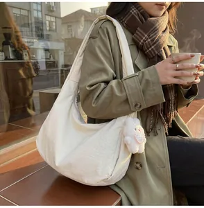 Large beige crescent hobo bag shown with a cute plush rabbit charm in an autumn street setting