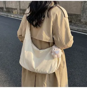 Detail of beige crescent canvas bag with a plush bunny charm on a wide shoulder strap