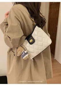 Detail of cream quilted crossbody bag with black trim and cute brown teddy bear charm