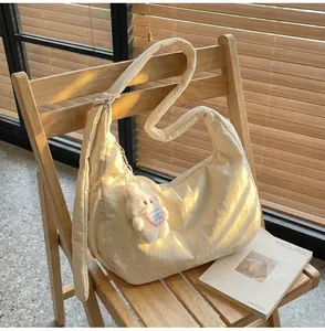 Beige quilted crescent shoulder bag with plush bunny charm in soft natural light
