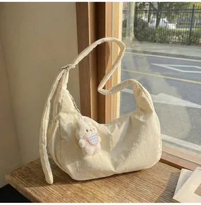 Detail of quilted off-white crossbody bag with plush bunny charm on a wooden bench