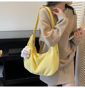 Detail of yellow nylon crescent bag with wide strap and white plush rabbit charm