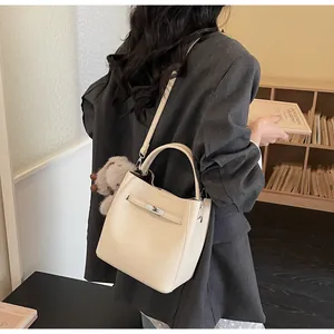 Dettaglio della borsa a secchiello beige con trama a grana, chiusura a scatto e ciondolo