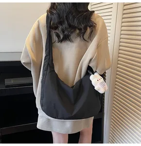 Detail of a black crescent crossbody bag with a white plush rabbit charm on a striped sweater