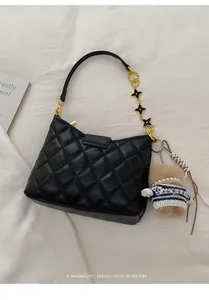 Close-up of black quilted leather crossbody bag with gold clover chain and teddy bear charm