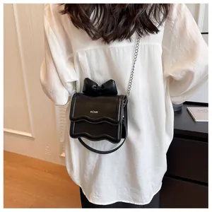 Detail of a black crossbody bag featuring a 3D bow, wavy edge, and silver chain strap